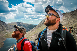 Two hikers looking up on a mountain while wearing Nöz colorful sunscreen on their nose. 